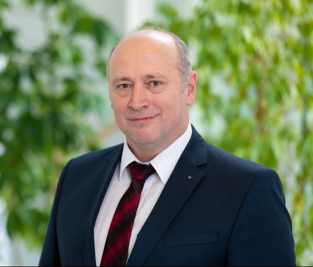 Porträtfoto von Georg Aron, Head of Solutions & Bid Management Commercial bei ISS Österreich, in einem Anzug vor einem Hintergrund mit Pflanzen.