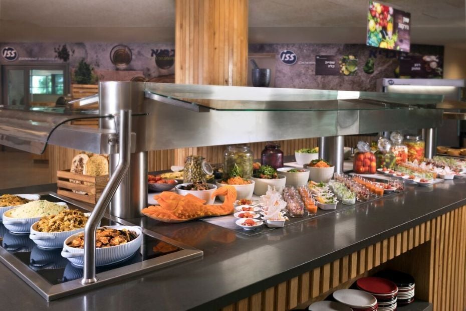 Große Buffet‑Theke mit Schalen, Gläsern und kleinen Tellern mit Salaten, Gemüsegerichten und Brot in einem gastronomischen Innenbereich