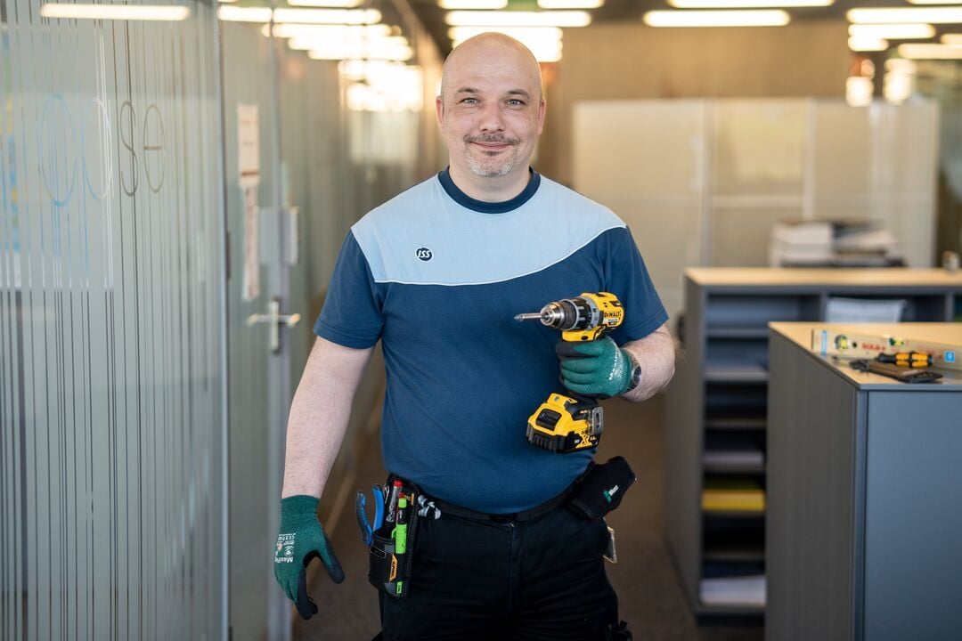 ISS Mitarbeiter in Arbeitskleidung hält einen Akkubohrer im Innenbereich eines Bürogebäudes