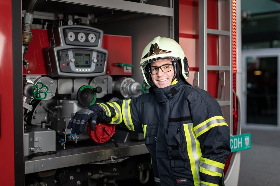 Person in Schutzkleidung steht vor einer technischen Anlage mit Manometern und Ventilen und berührt ein Bedienelement