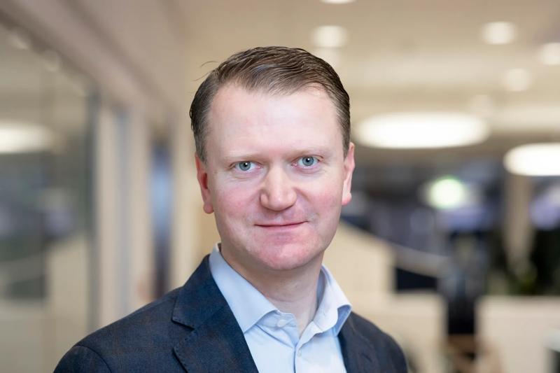 Kasper Fangel im Porträt vor neutralem Hintergrund, lächelt und blickt in die Kamera