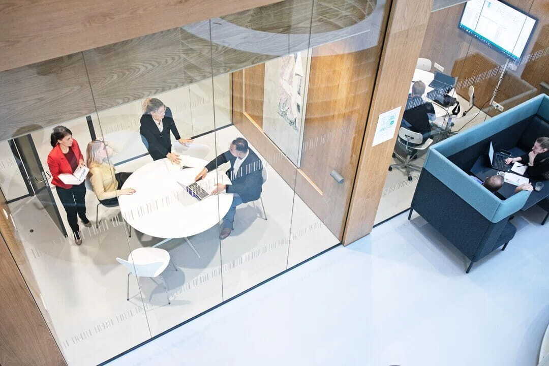 Teammeeting in modernem Büro mit mehreren Personen an einem Tisch und parallel genutzten Arbeitsbereichen
