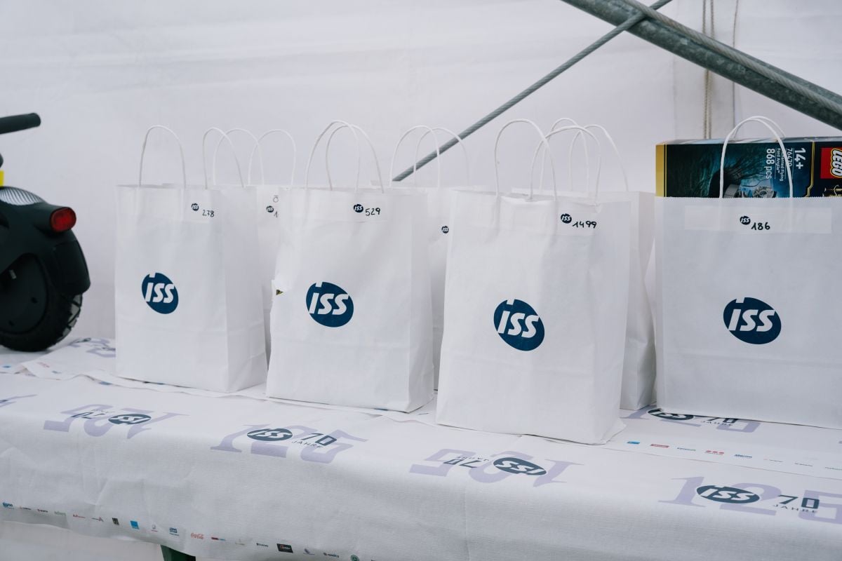 Mehrere weiße Geschenktaschen mit ISS‑Logo stehen auf einer Tischdecke mit „70 Jahre ISS“-Branding und verschiedenen Partnerlogos.