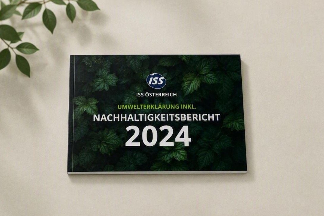 Der Nachhaltigkeitsbericht 2024 von ISS Österreich als hochwertige Publikation im Querformat auf hellem Untergrund mit dezenten grünen Blättern als Akzent.
