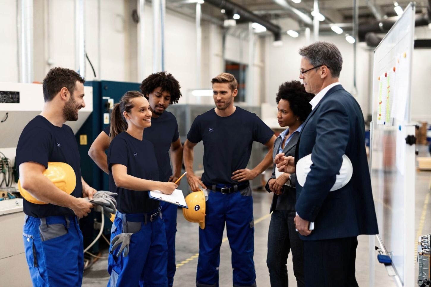 Mitarbeitende und Führungskräfte besprechen gemeinsam Arbeitsabläufe und Projekte in einer modernen Produktionsumgebung.