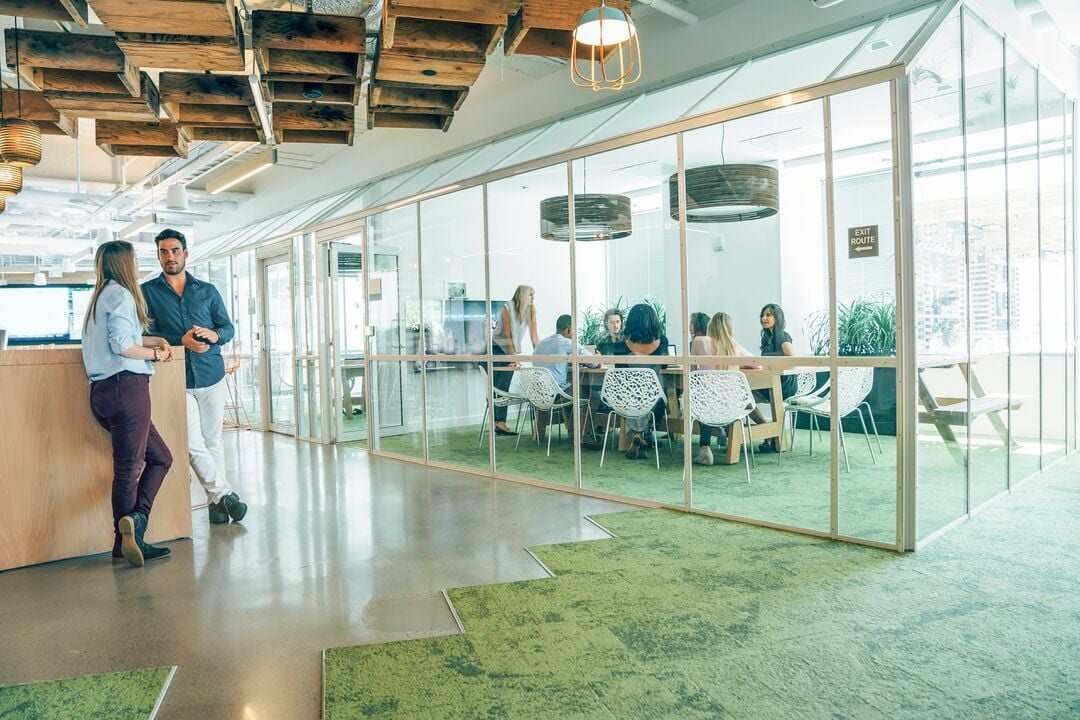 Modernes Büro mit offenem Raumkonzept und verglastem Meetingraum, in dem ein Team zusammenarbeitet und Besprechungen durchführt