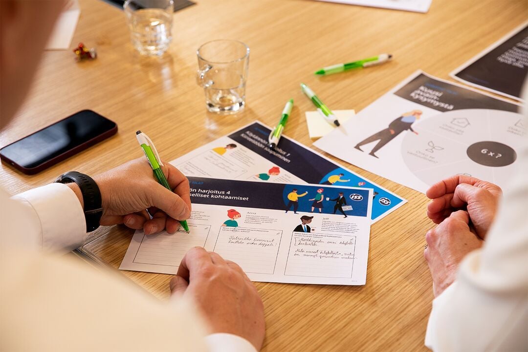Mitarbeitende bearbeiten gemeinsam Schulungsunterlagen und dokumentieren Inhalte während eines Workshops.