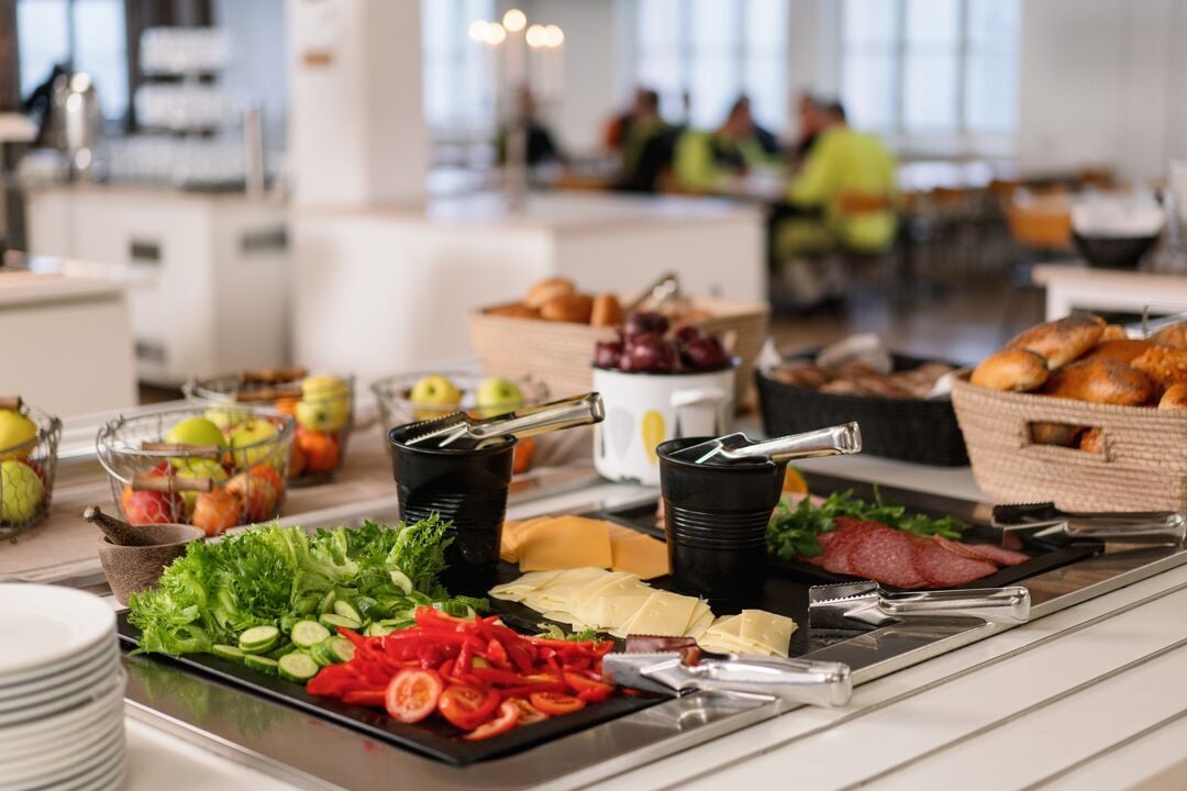 Buffet mit Käse-, Wurst- und Gemüseplatten, Servierzangen, Brotkörben und Obstschalen in einem gastronomischen Innenbereich