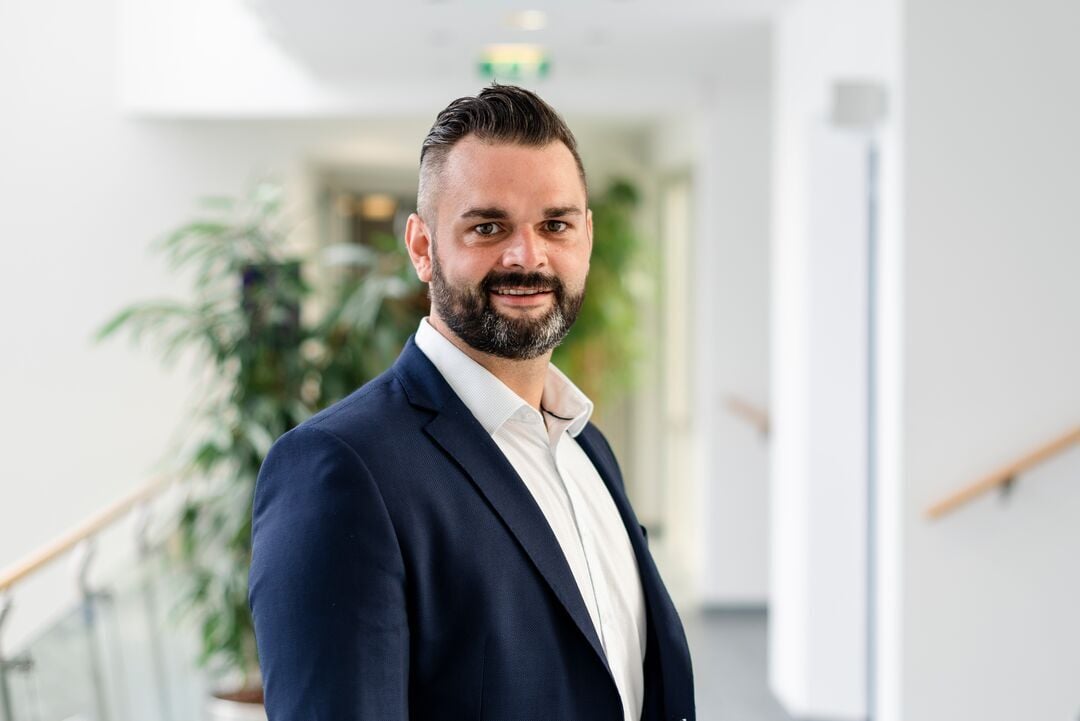 Bernd Steinreiber im Porträt in Businesskleidung vor Innenraum, lächelt und blickt in die Kamera