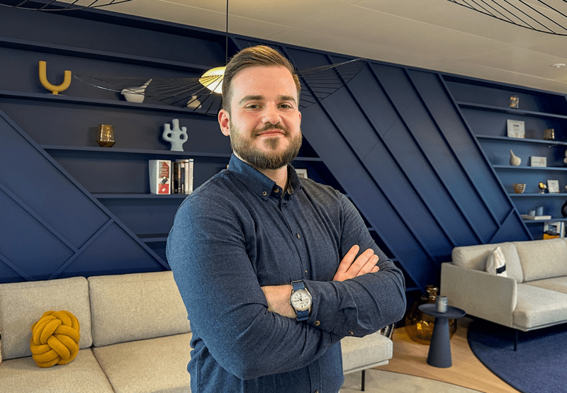 Porträtfoto von Christoph Hagmann, Specialist Communication bei ISS Österreich, vor einer modernen Regalwand im Büro.