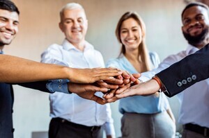 Diverses Team von Mitarbeitenden legt die Hände übereinander als Symbol für Zusammenarbeit, Vertrauen und Teamgeist im Unternehmen