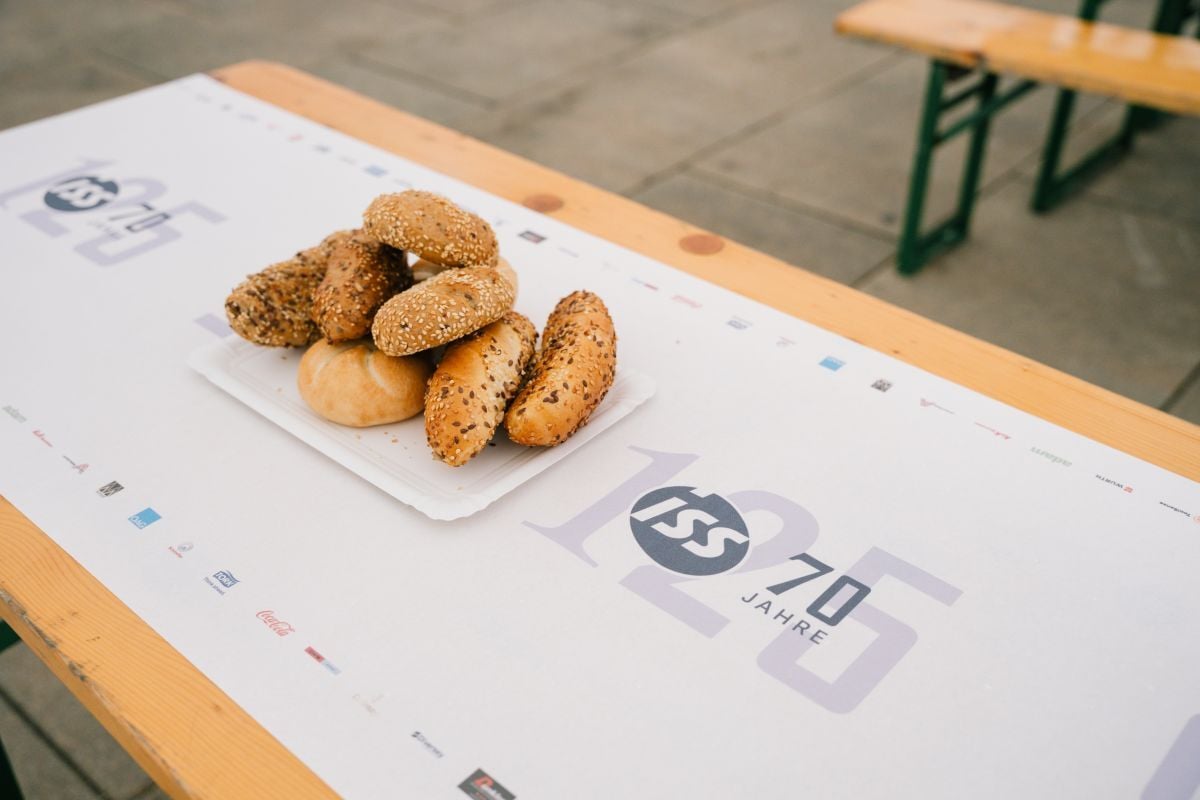 Gebäck auf einer Tischdecke mit „70 Jahre ISS“-Branding und mehreren Logos, platziert auf einem Holztisch.